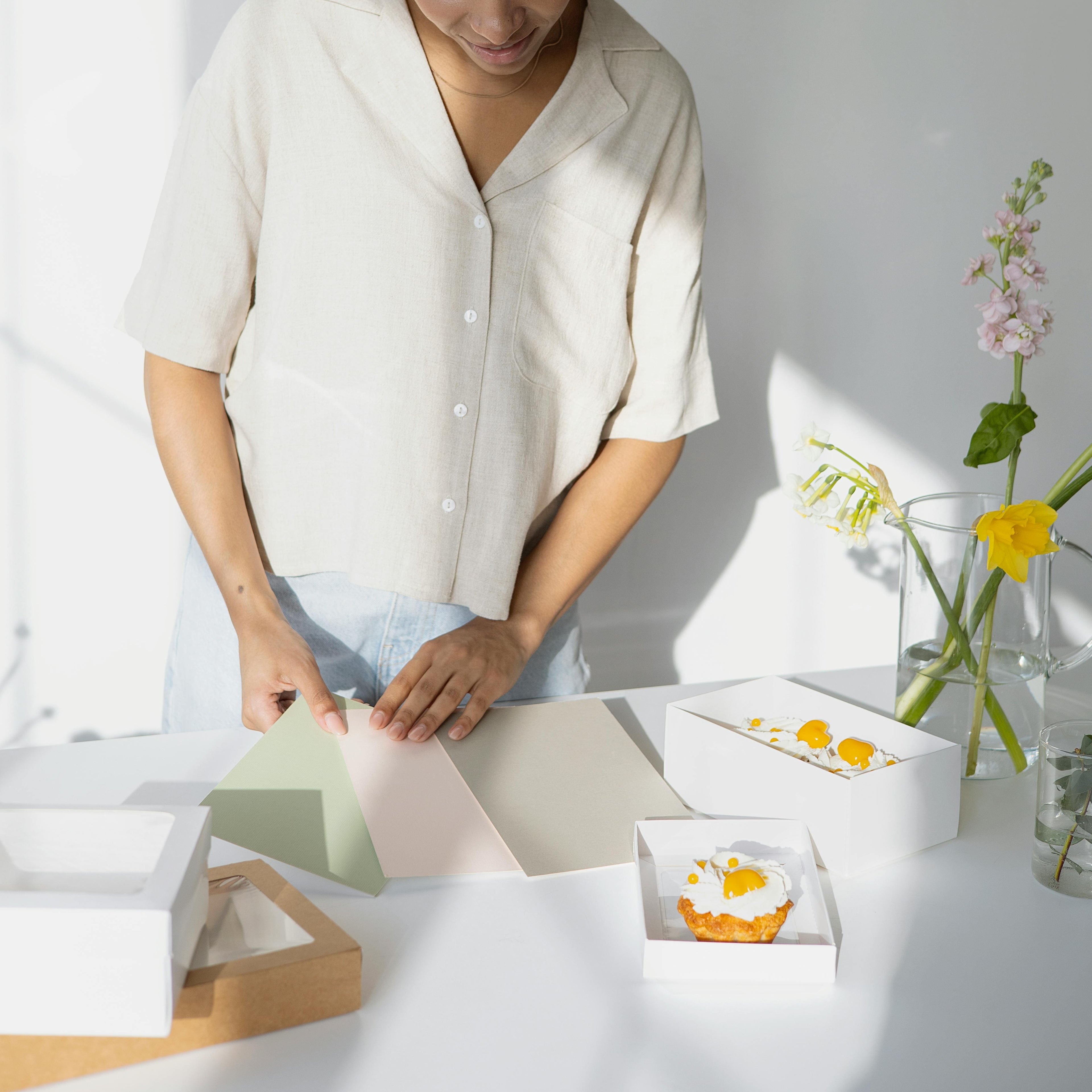 Woman in a white shirt arranging items on a table with a clock and flowers in the background